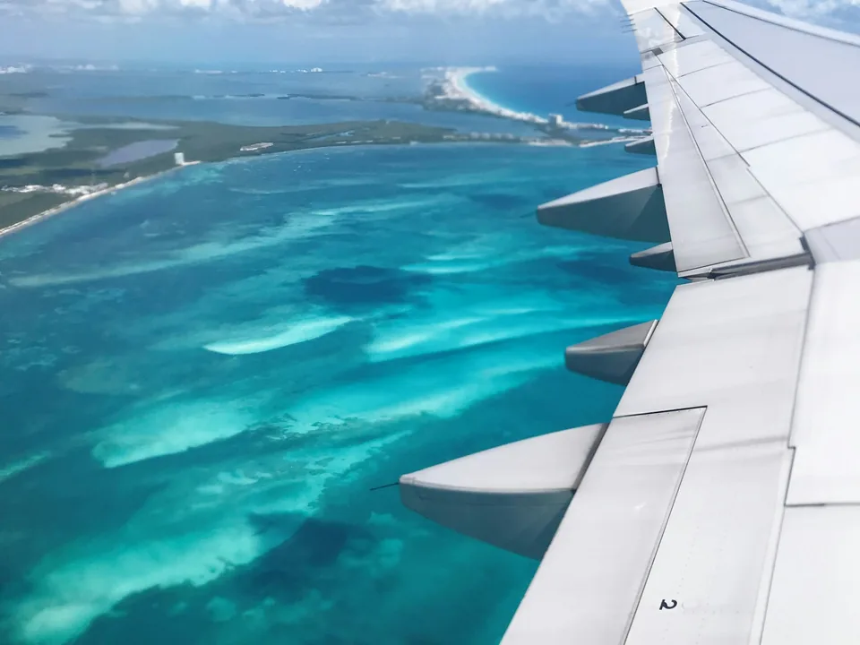 Aircraft wing above turquoise water on approach to an island
