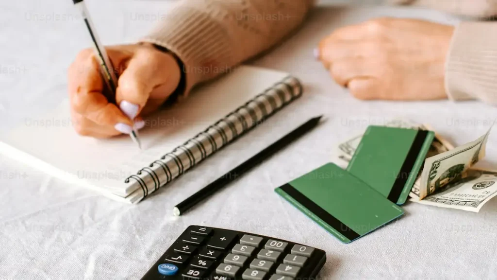 A woman writing on a notepad beside a calculator and cash, checking visa income requirements