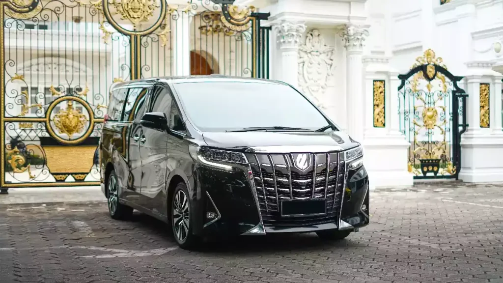 A black Toyota Alphard luxury transfer van waiting at an ornate Balinese gate